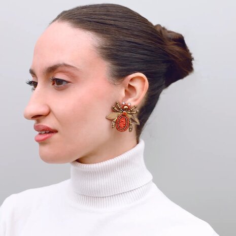 Persoon draagt gouden vlieg oorbellen met beige glaskraaltjes detail