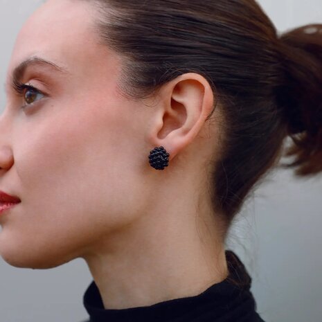 Persoon draagt kleine gouden bol oorstekers met kraalstructuur